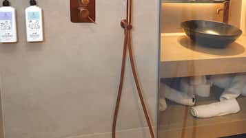 Ein modernes Badezimmer mit Dusche, Waschbecken und Spiegel. An der Wand befinden sich zwei Shampooflaschen und eine Duschgelflasche.