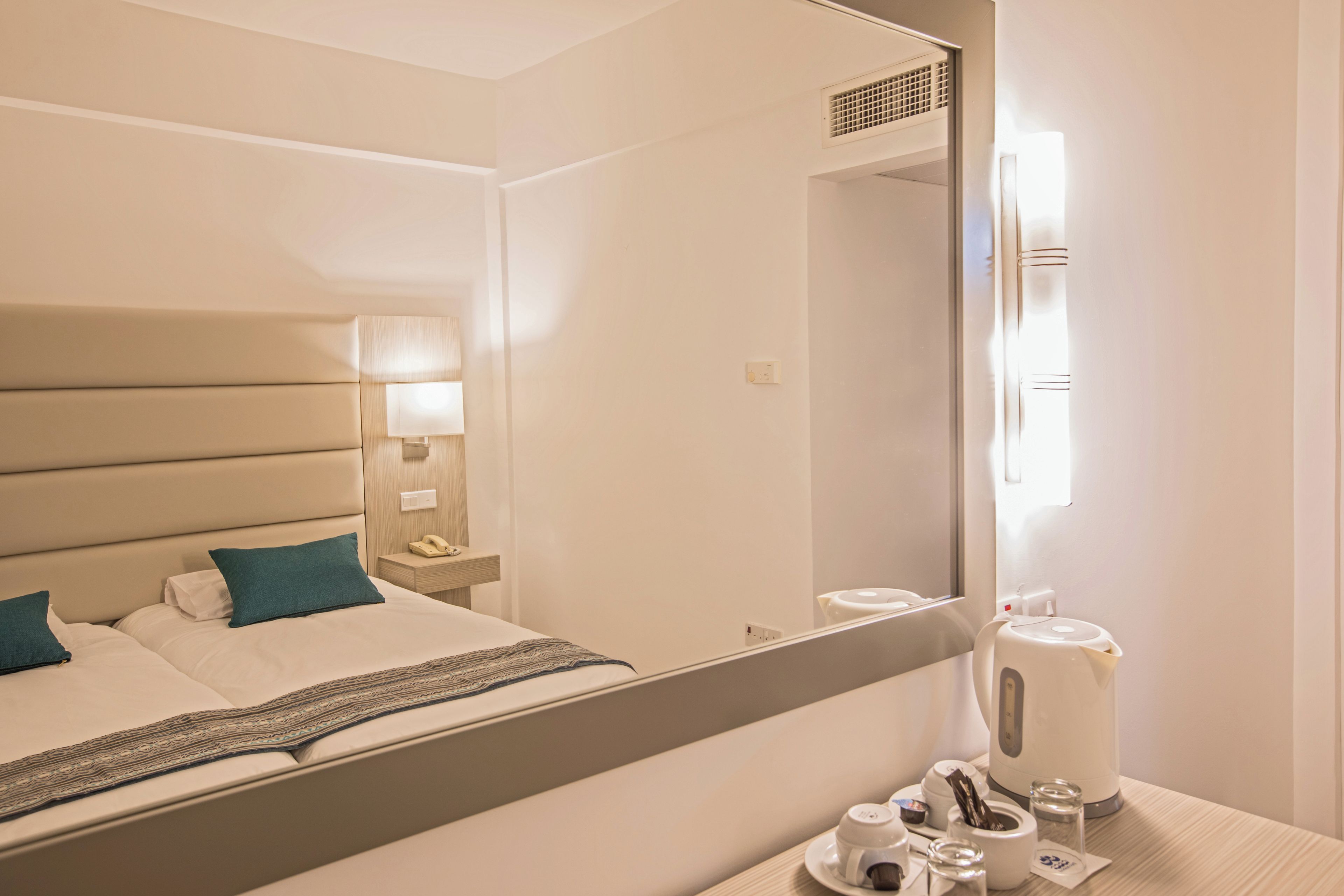 Habitación de hotel con cama, mesita de noche, lámpara y un espejo que refleja el cuarto.