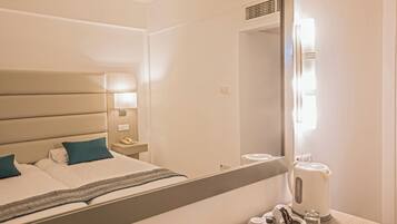 Habitación de hotel con cama, mesita de noche, lámpara y un espejo que refleja el cuarto.