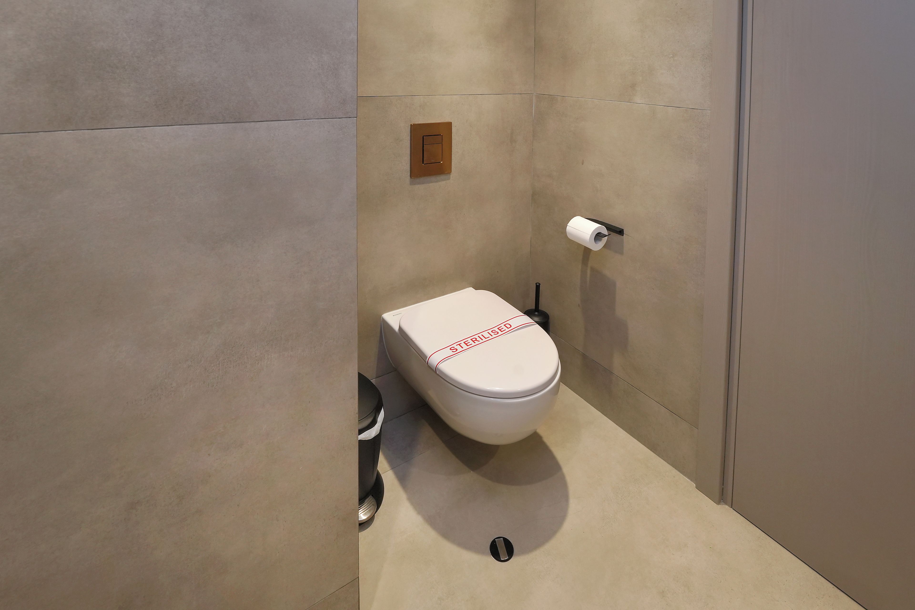 Des toilettes modernes avec une étiquette indiquant « STÉRILISÉ », une poignée de chasse d’eau et un porte-rouleau de papier toilette.