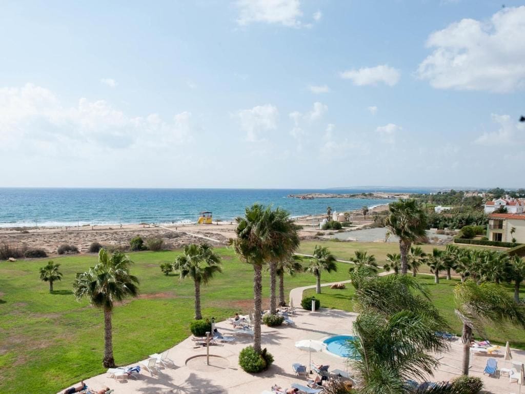Un complexe hôtelier doté d’une piscine, de palmiers et offrant une vue sur la mer.