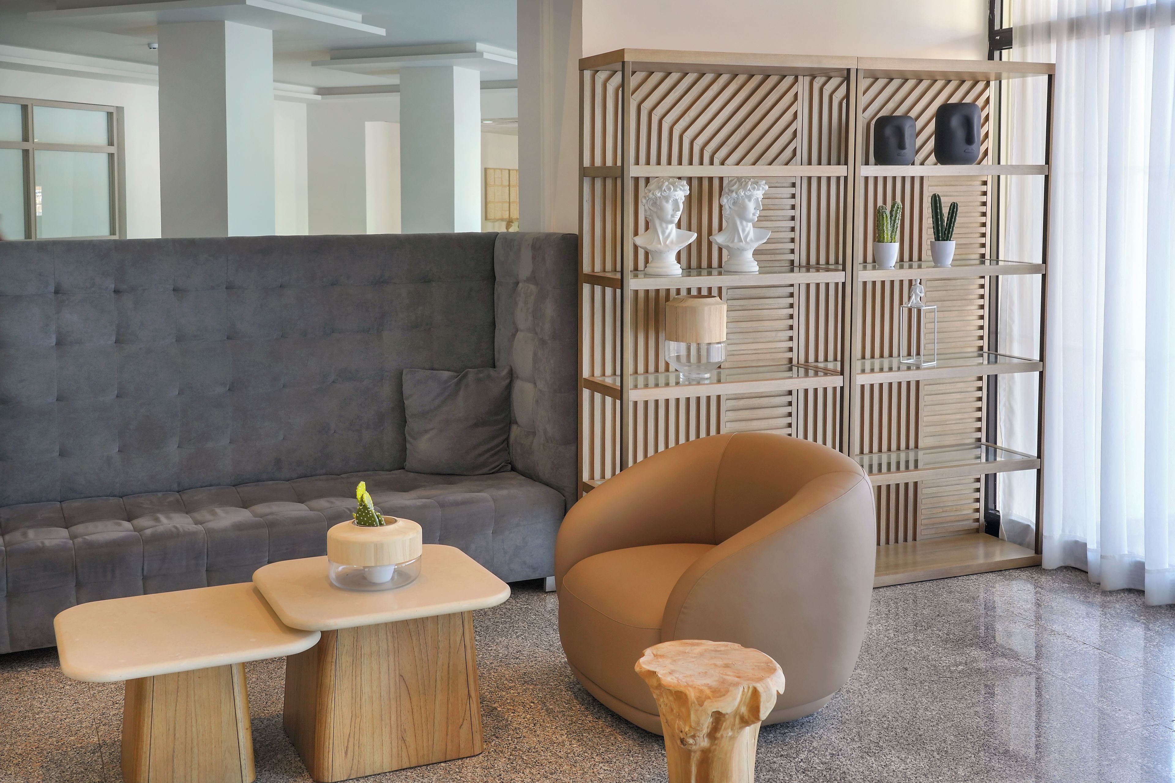 Una sala moderna con un sofá gris, una mesita de madera, un taburete redondo de madera y una estantería empotrada con objetos decorativos.