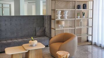 Una sala moderna con un sofá gris, una mesita de madera, un taburete redondo de madera y una estantería empotrada con objetos decorativos.