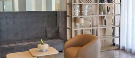 Una sala moderna con un sofá gris, una mesita de madera, un taburete redondo de madera y una estantería empotrada con objetos decorativos.