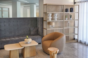 Una sala moderna con un sofá gris, una mesita de madera, un taburete redondo de madera y una estantería empotrada con objetos decorativos.