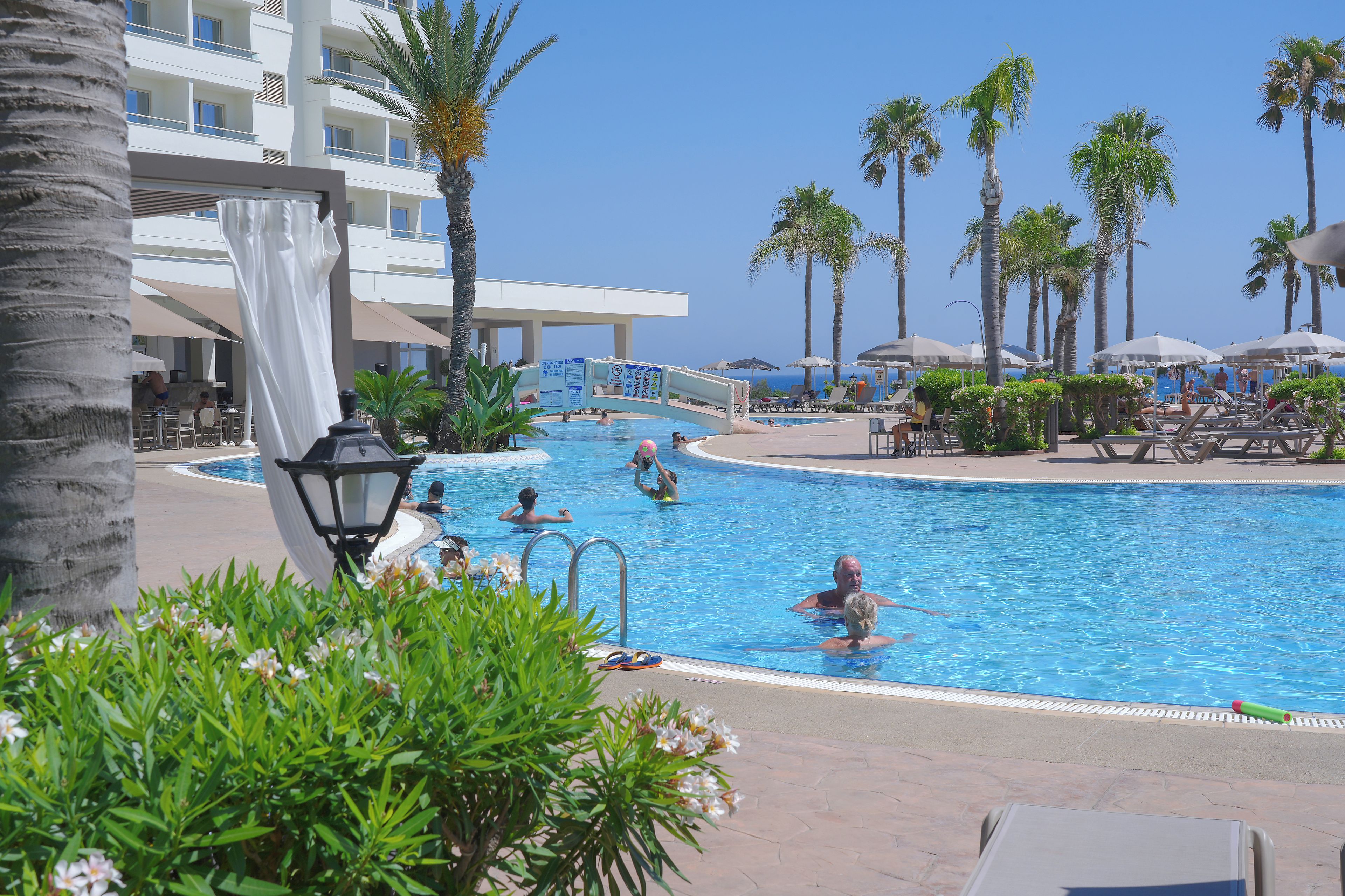 A swimming pool with a clear blue sky, surrounded by palm trees and lounge chairs.