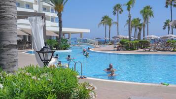 A swimming pool with a clear blue sky, surrounded by palm trees and lounge chairs.