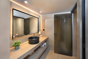 Un baño moderno con un espejo grande, un lavabo sobre encimera y una cabina de ducha de vidrio.