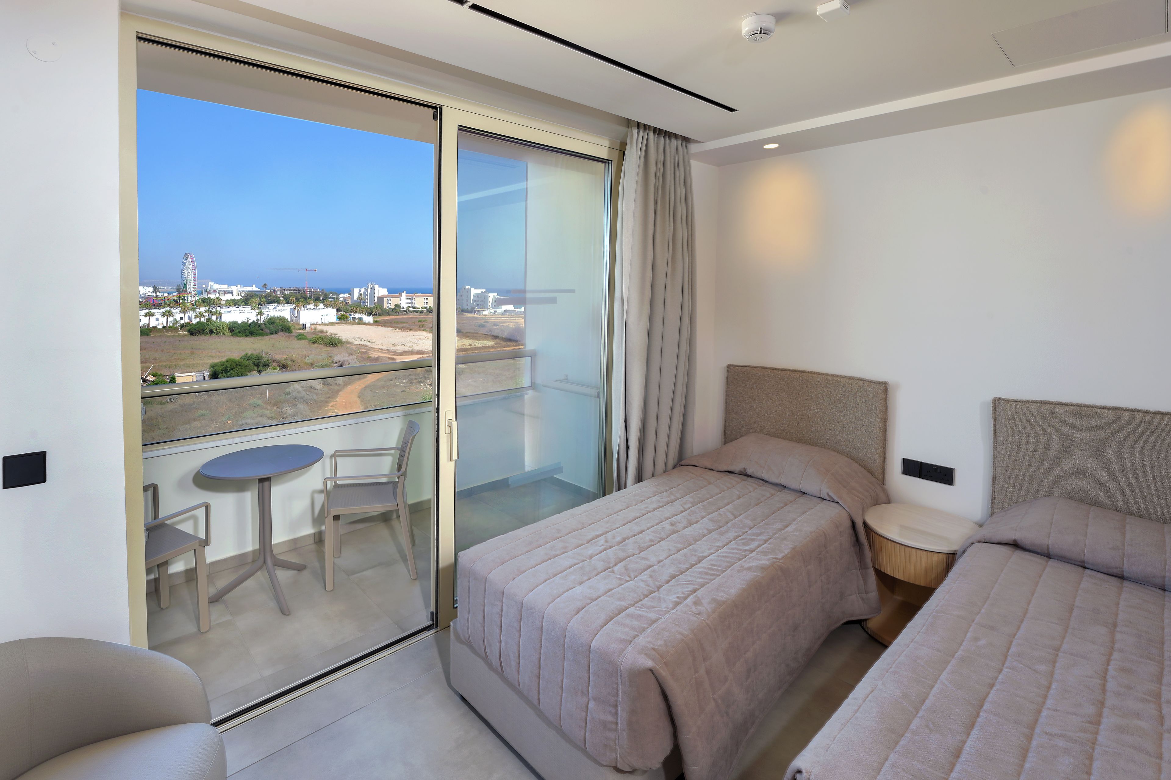 A hotel room with a balcony, a bed, a chair, and a small table.