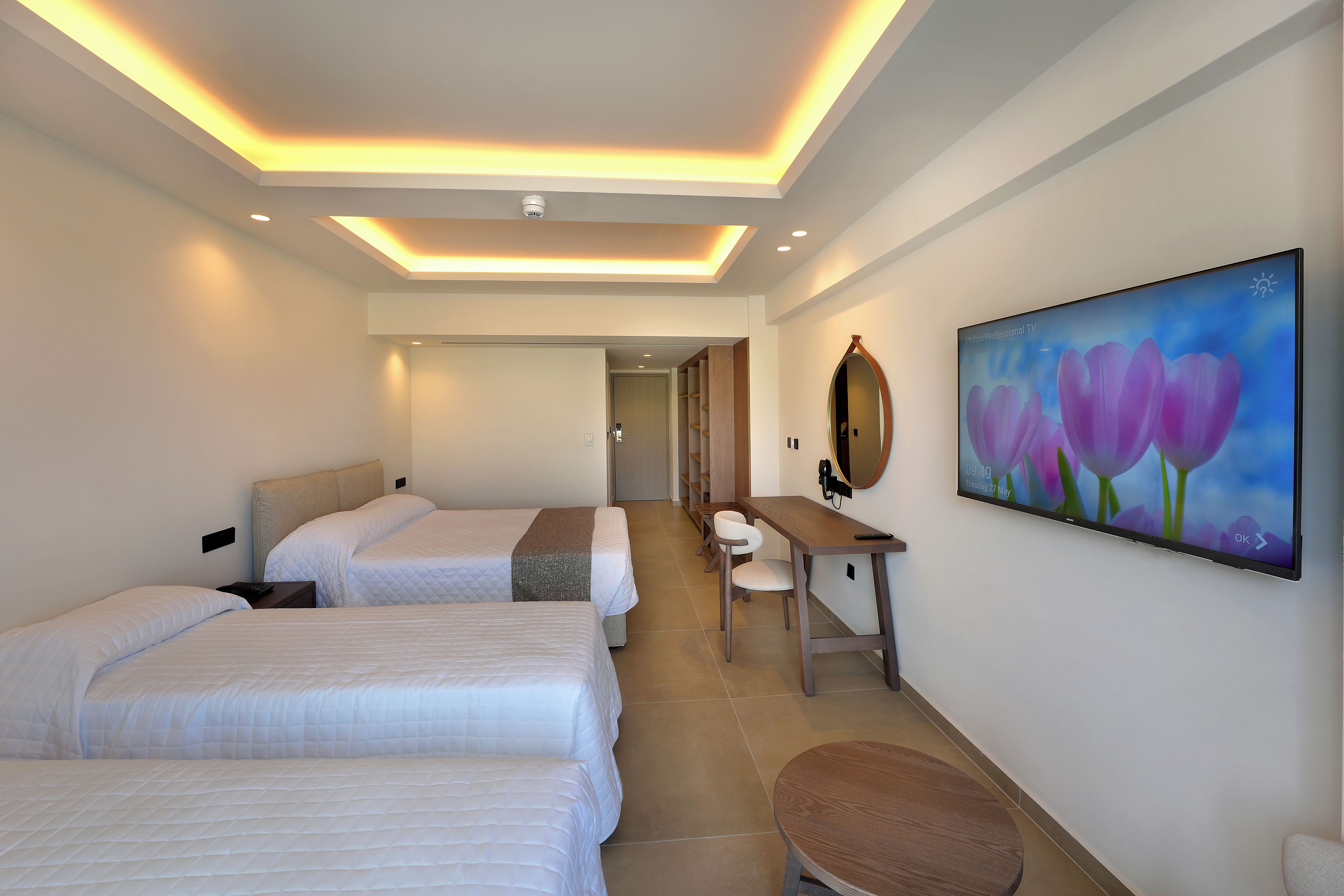 Quarto de hotel com duas camas, uma escrivaninha, uma cadeira, televisão de tela plana e um quadro na parede.
