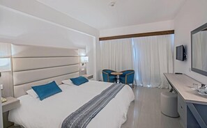 A hotel room with a large bed, bedside tables, a desk with a chair, a TV, and a window with curtains. - NELIA SEA BREEZE HOTEL (Ayia Napa)
