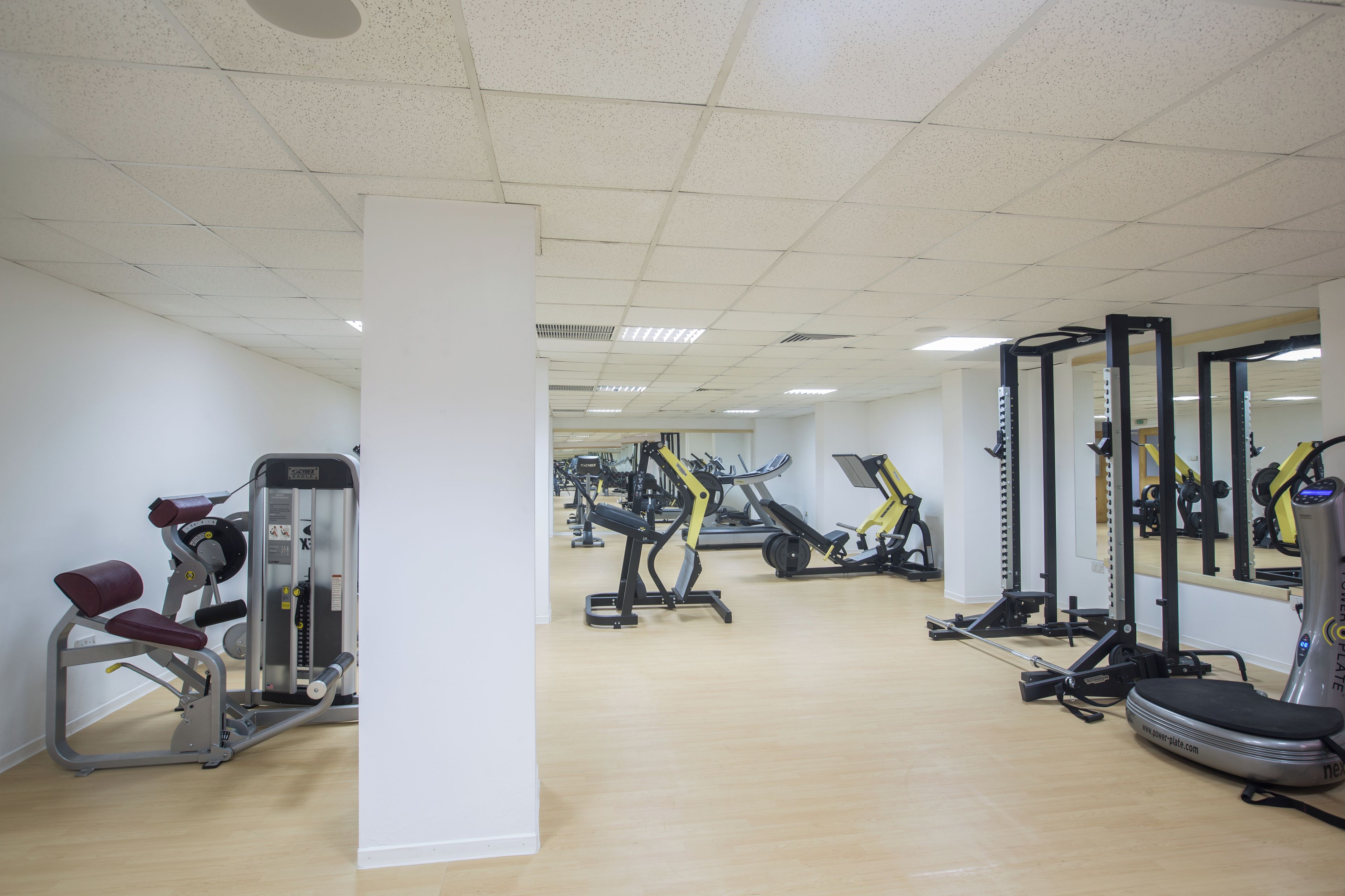A gym with various exercise machines, a wooden floor, and white walls.