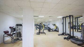 A gym with various exercise machines, a wooden floor, and white walls.