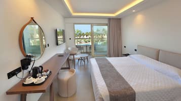 Habitación de hotel con cama, escritorio, teléfono, cafetera, una silla, una mesita y vista a una piscina y palmeras a través de la ventana.
