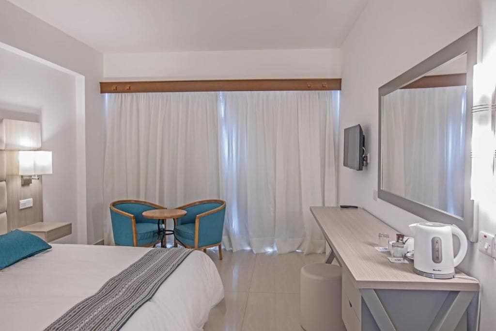 Habitación de hotel con cama, escritorio, silla, televisión y tetera.
