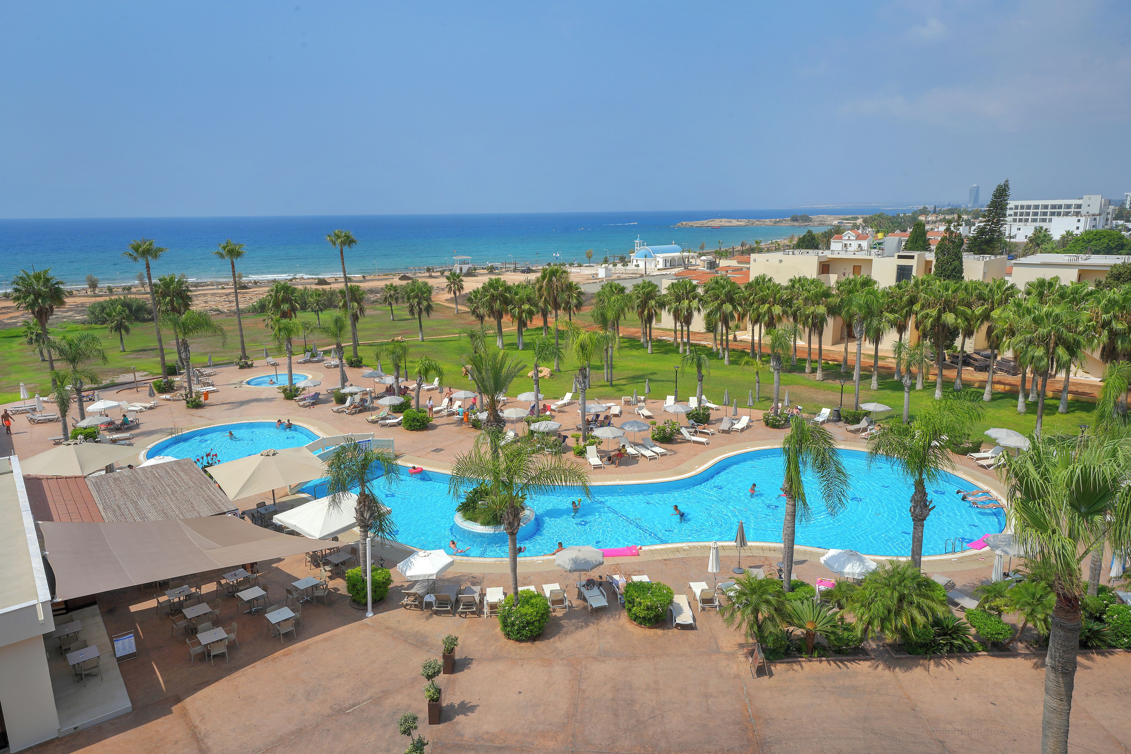 Een resort met een zwembad, ligbedden en palmbomen.