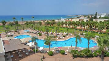 Een resort met een zwembad, ligbedden en palmbomen.