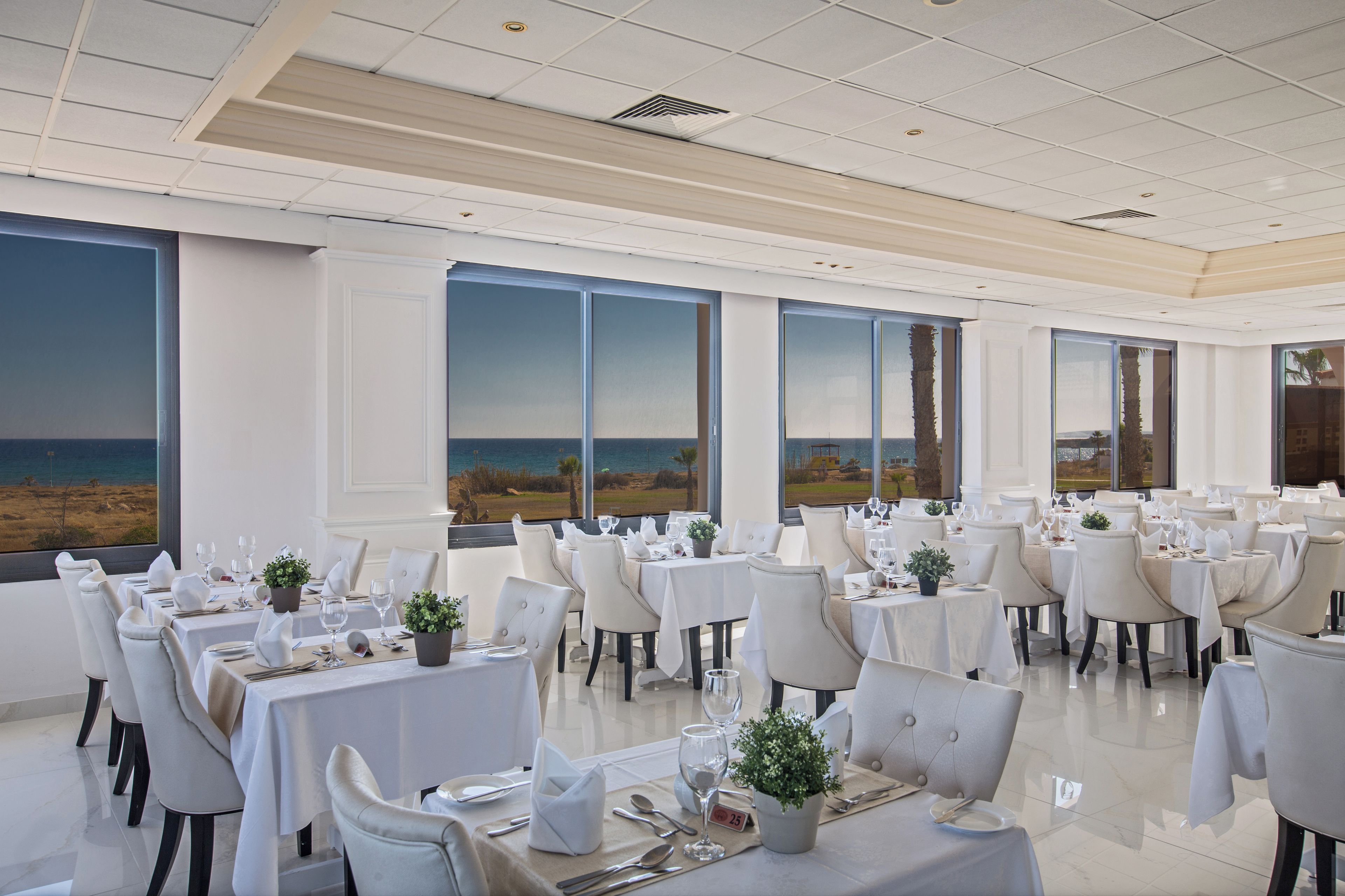 Un comedor con mesas dispuestas para el servicio, ventanas amplias con vista a la playa y un interior moderno y cuidado.