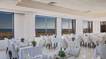 Un comedor con mesas dispuestas para el servicio, ventanas amplias con vista a la playa y un interior moderno y cuidado.