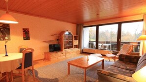 Un soggiorno accogliente con soffitto in legno, un tavolo da pranzo con sedie, un divano, una libreria e un'ampia finestra con vista.