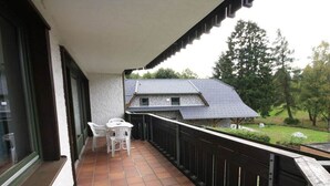Un balcone con tavolo e sedie, vista su una casa e ringhiera in legno.