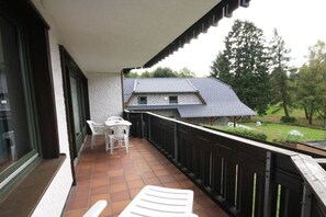 Een balkon met een tafel en stoelen, uitzicht op een huis en een houten hekwerk.