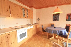 Een keuken met houten kasten, een fornuis en een eethoek met een tafel en stoelen.