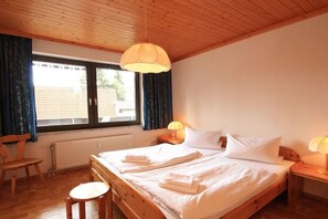 Een slaapkamer met een houten bed, twee nachtkastjes met lampen, een raam met gordijnen en een radiator.