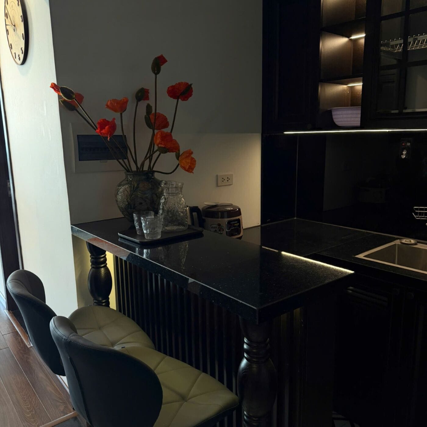 A modern kitchen with a black countertop, a vase with red flowers, and a bar stool.