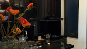 A kitchen with dark wooden cabinets, a black countertop, a vase with orange flowers, and a clear glass pitcher.