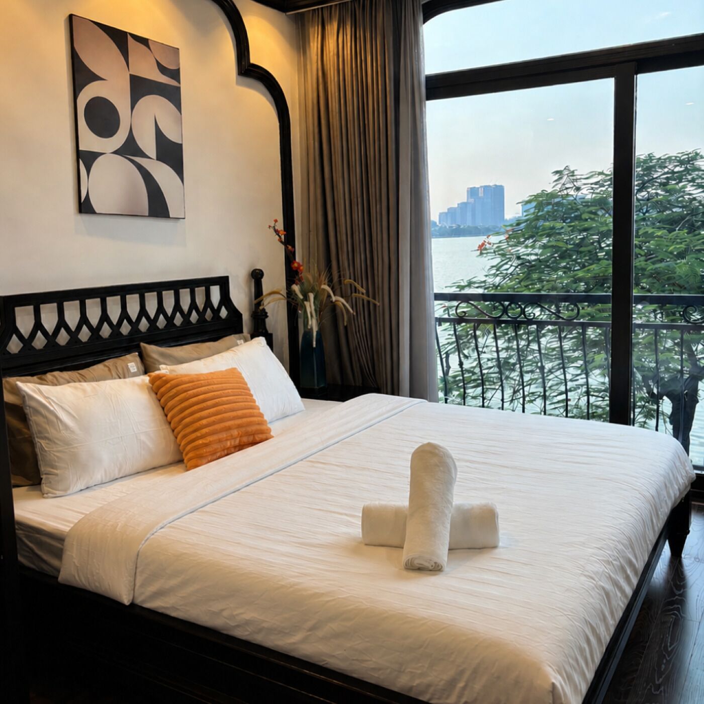 A hotel room with a bed, a view of the city through large windows, and a decorative wall piece.