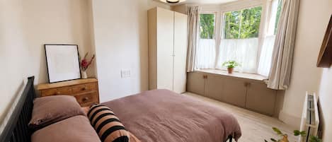 A bedroom with a bed, bedside table, lamp, window with curtains, and a potted plant.