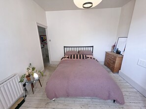 A bedroom with a bed, dresser, radiator, and a potted plant. - Charming 2BDR Victorian Home in Leyton (Greater London)
