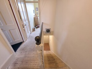 A hallway with a wooden floor, a white door, and a staircase with a handrail. - Charming 2BDR Victorian Home in Leyton (Greater London)