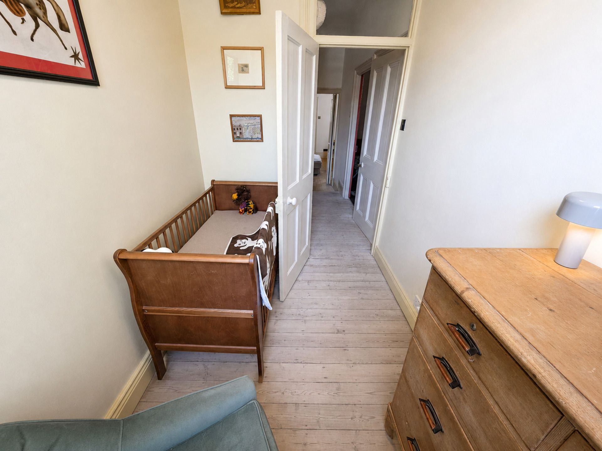 Un couloir étroit avec un berceau en bois, une commode et une lampe.