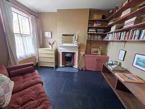 A cozy living room with a fireplace, a bookshelf, and a comfortable sofa. - Charming 2BDR Victorian Home in Leyton (Greater London)