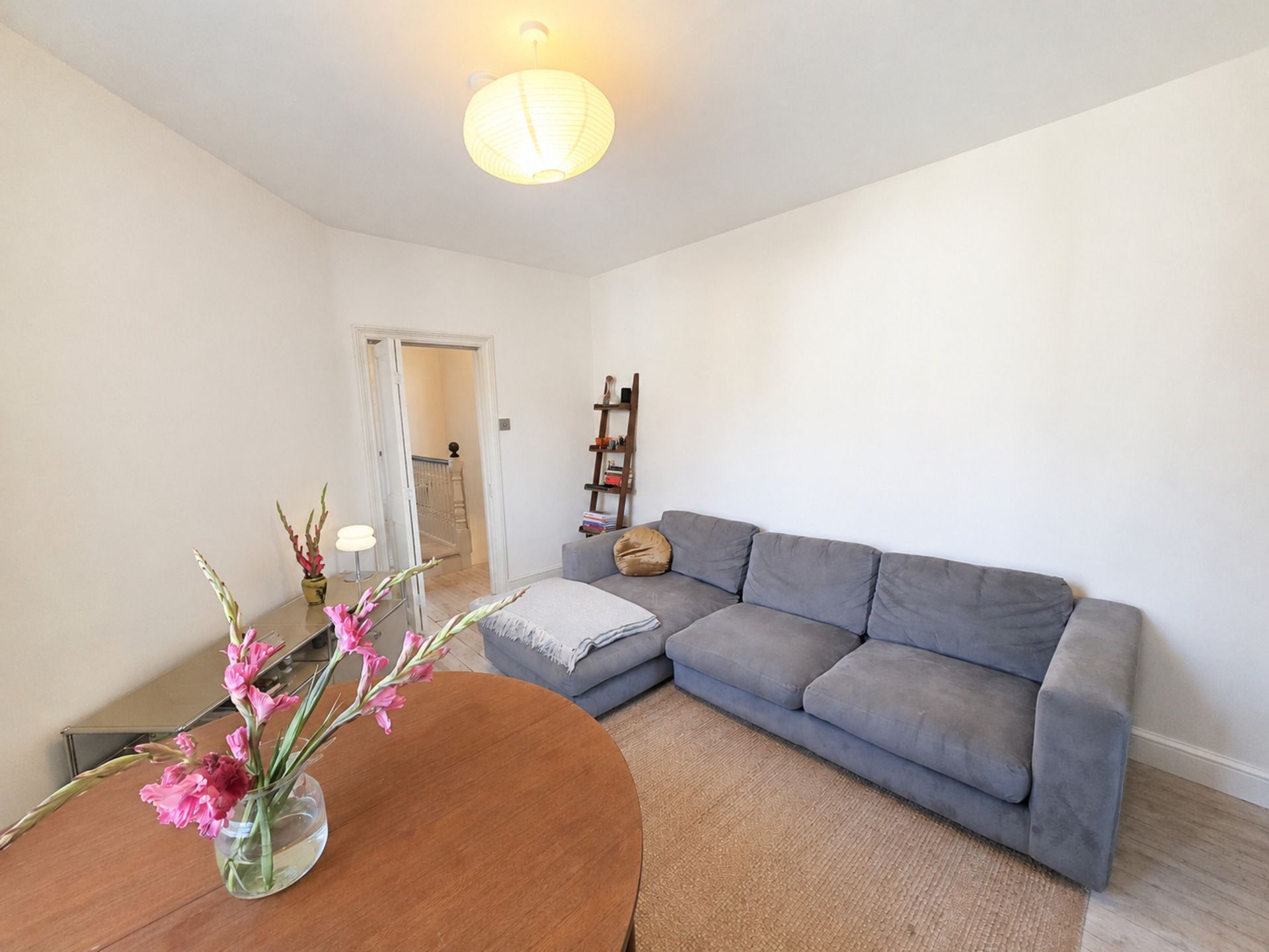 A living room with a grey sofa, a wooden coffee table with a vase of flowers, and a ceiling light fixture.