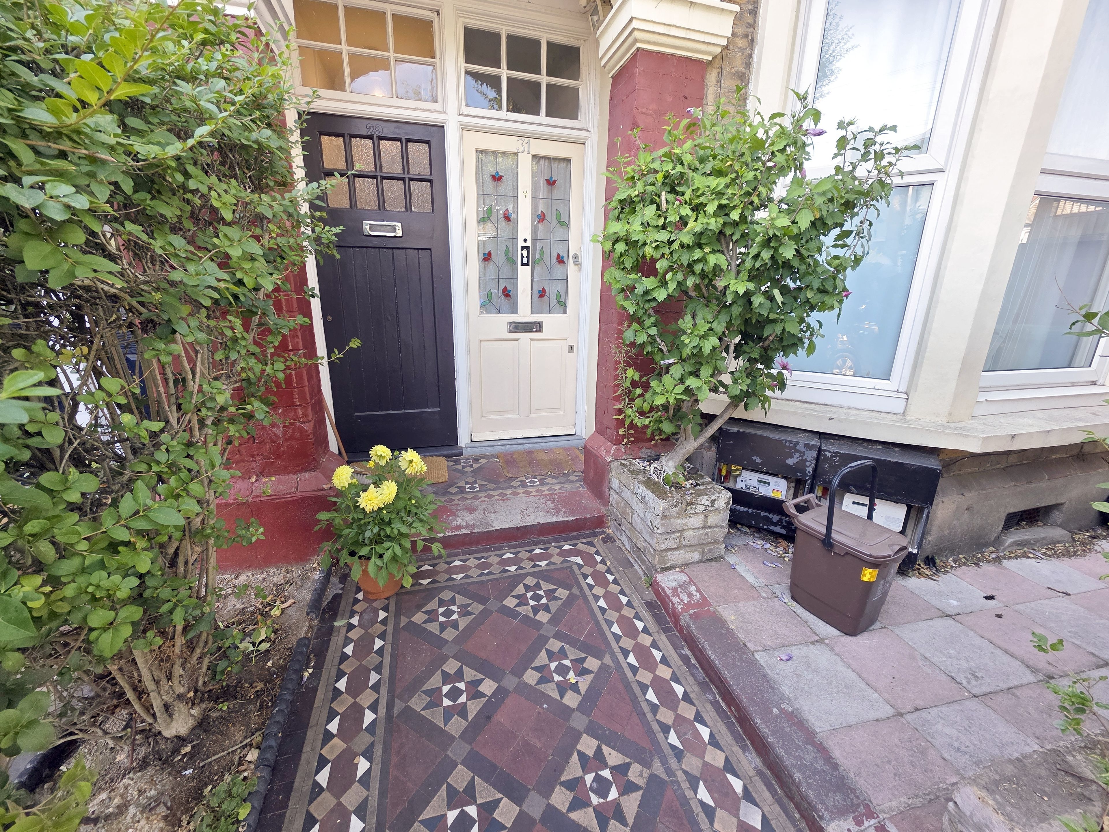 Entrada frontal com porta preta, piso de azulejos e caixa de correio.