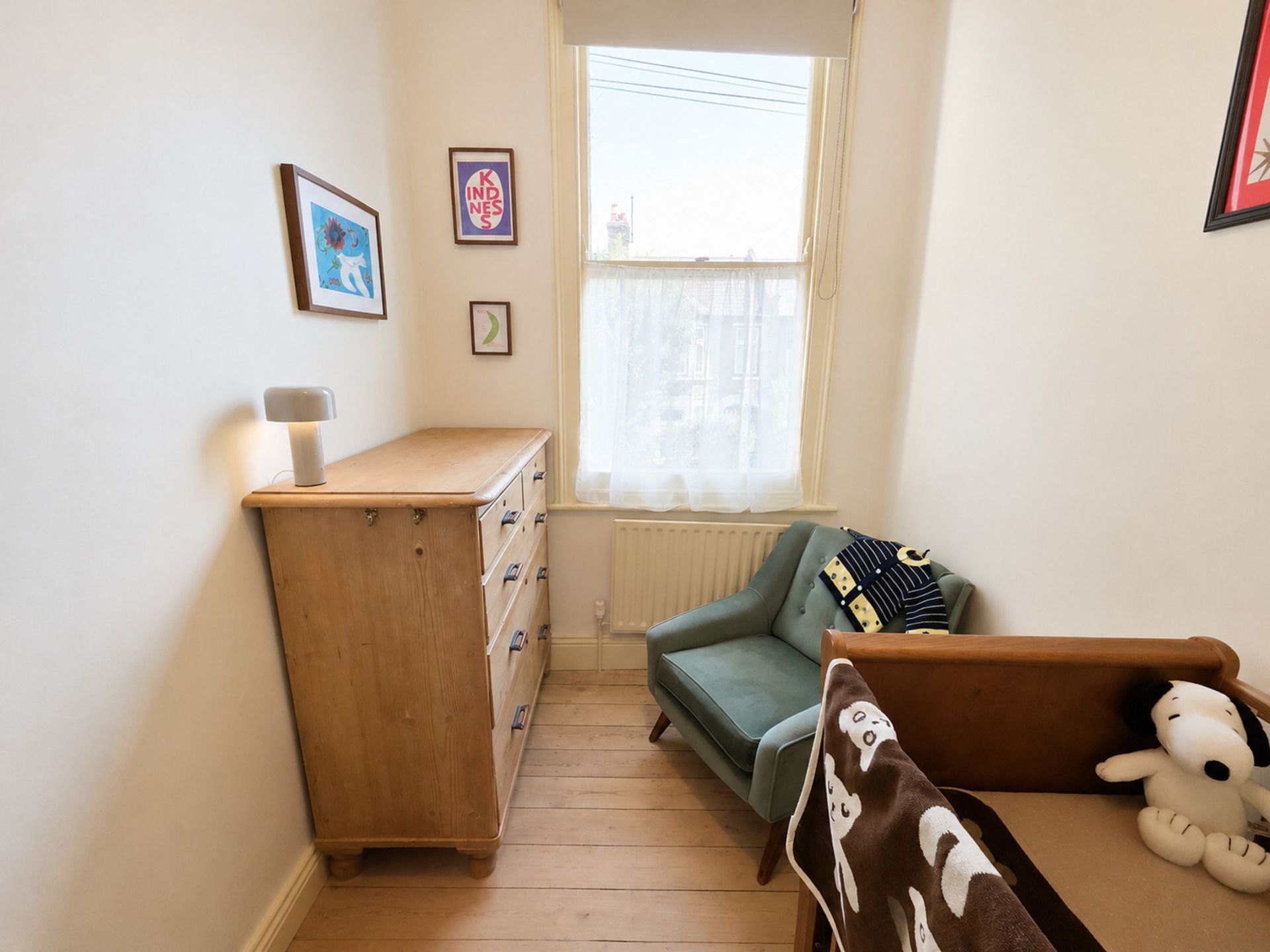 Una habitación con un aparador de madera, un sofá verde, un ventanal con cortinas traslúcidas y una pared con cuadros enmarcados.