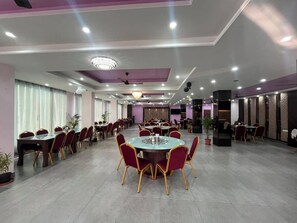 A spacious dining area with multiple round tables and chairs, ceiling fans, and recessed lighting.