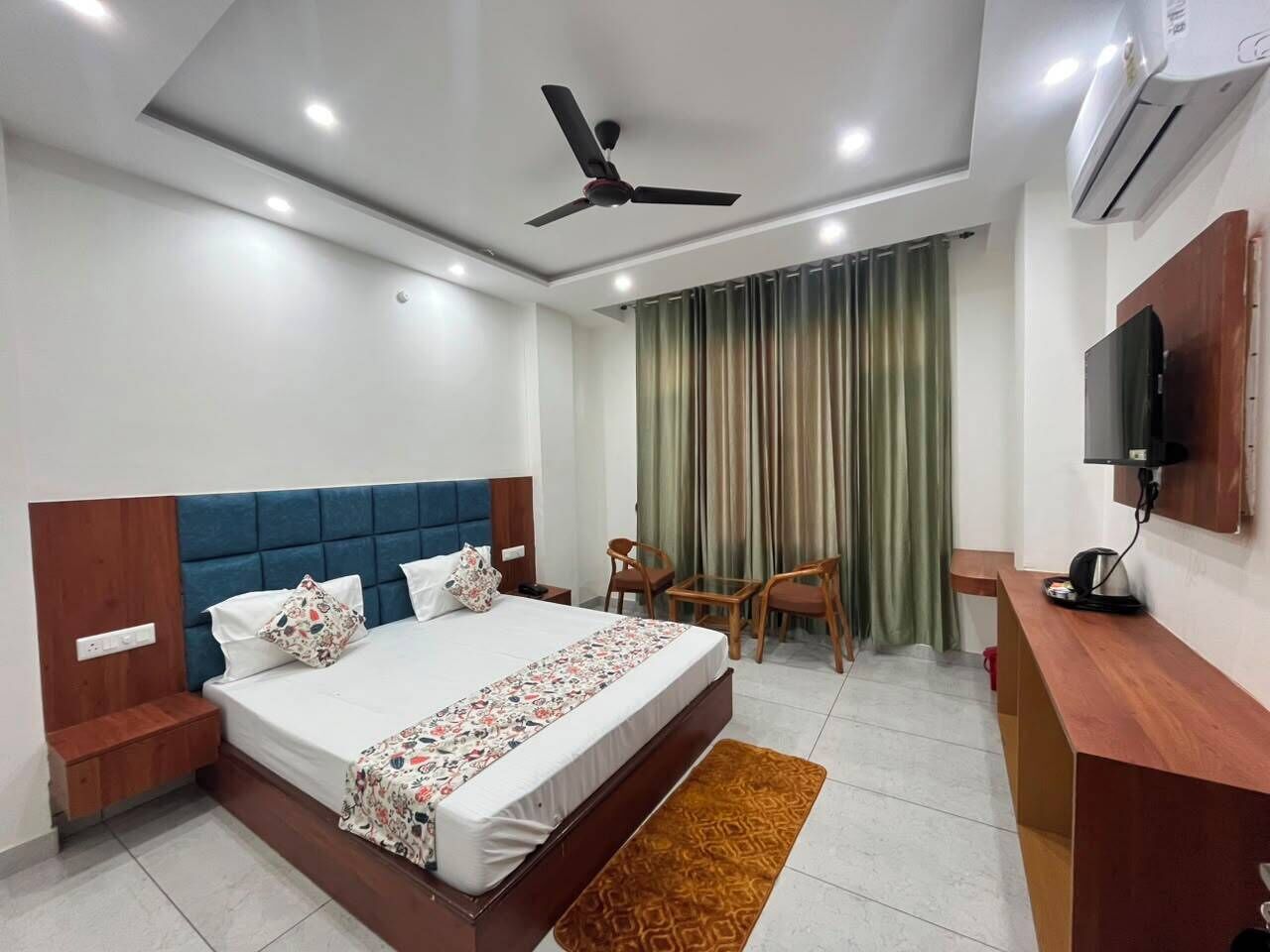 Quarto de hotel com cama, escrivaninha, cadeira, televisão e ventilador de teto.