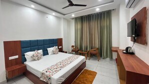 A hotel room with a bed, a desk, a chair, a TV, and a ceiling fan.