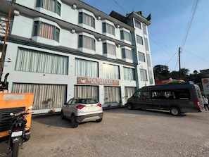 A multi-story building with a sign for 'New Green Valley Hotel & Restaurant.' There are parked vehicles in front, including a car and a van.