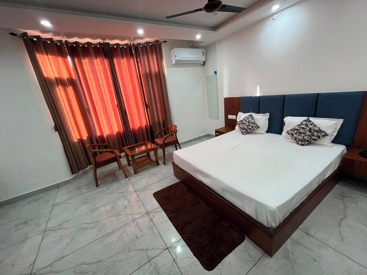 A bedroom with a bed, two chairs, a nightstand, a ceiling fan, and an air conditioning unit.