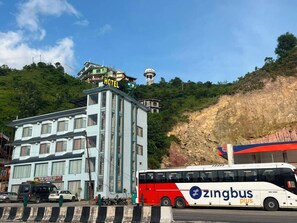 A hotel building with a sign that reads 'HOTEL' and a bus with 'zingbus' branding on the street. - New Green Valley Hotel And Restaurant (Sundarnagar)