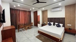 A hotel room with a bed, a desk, a chair, a television, and an air conditioning unit.