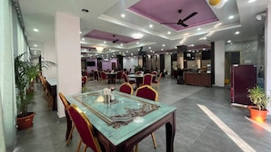 A spacious hotel lobby with multiple dining areas, ceiling fans, and potted plants.
