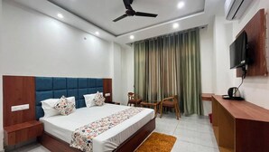 A hotel room with a bed, a desk, a chair, a television, and an air conditioning unit.