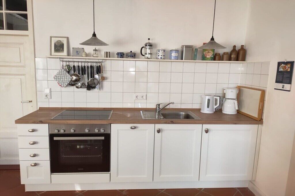 Una cocina con armarios blancos, horno empotrado, lavamanos y encimera con diversos utensilios de cocina.