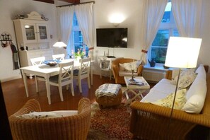 A furnished living room with a dining area, a television, and a window with curtains. - Hof Homfeld Apartment 2 (Jemgum)